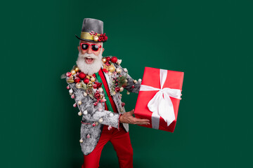 Portrait of elderly charismatic man hold giftbox decorated outfit cylinder hat isolated on dark green color background