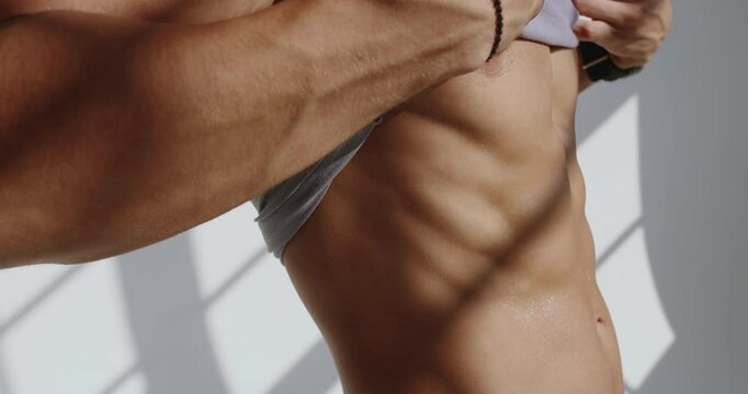 Athletic Young Man Training in Studio, Showing Off Muscular Torso. A 23-year-old athletic man lifts his shirt, revealing a toned torso during a fitness session in a bright studio.