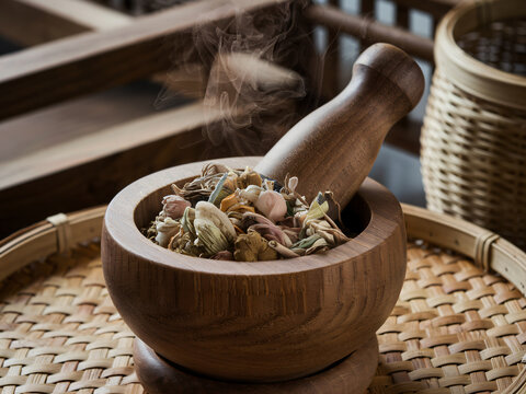 A wooden mortar and pestle filled with herbs, releasing aromatic smoke, evokes sense of tradition and natural healing. This image captures essence of culinary and medicinal practices