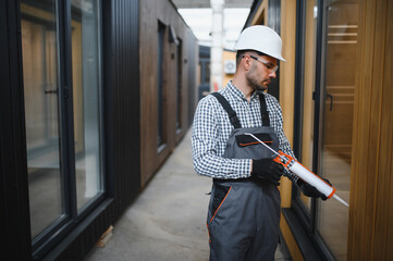 A worker is applying polyurethane foam to fill gap between sash and window frame in prefabricated...