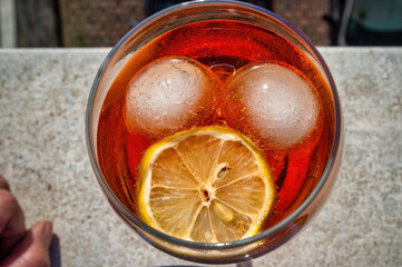 Aperol spritz cocktail seen from above, with ice and lemon forming a face