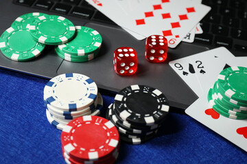 Poker chips, laptop, playing cards and dices on blue table. Online game