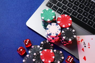 Poker chips, laptop, playing cards and dices on blue table, above view. Online game