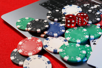 Poker chips, laptop and dices on red table, closeup. Online game