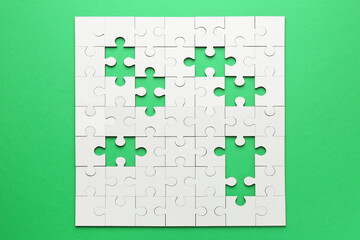 White puzzle with missing pieces on green background, top view