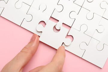 Woman solving white puzzle on pink background, closeup