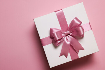 Gift box with bow on dusty pink background, top view