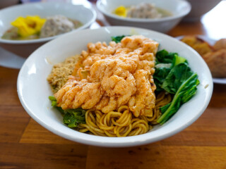 A bowl of sweet Yamin noodles with green pakcoy vegetables and fried wonton crackers. The broth, dumplings and meatballs are served separately