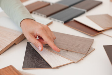 Woman choosing wooden flooring among different samples at table, closeup