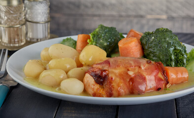 Chicken breast wrapped in bacon with potatoes and vegetables with a chicken gravy.