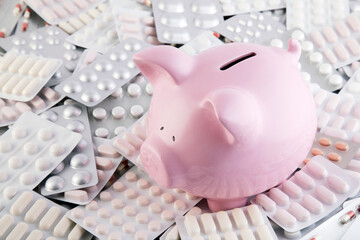 Pink piggy bank on big heap of many various pills and tablets packs for savings and healthcare...