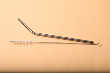 Metal drinking straw and cleaning brush on beige background, top view