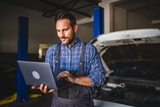 Adult man car mechanic work on laptop in garage with car in background
