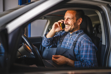 Car mechanic talk on mobile phone while sit in car during repair