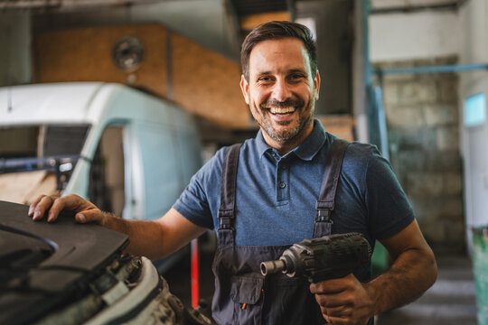 Happy car mechanic with power tool in a bright auto workshop