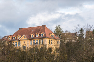 Historisches Schulhaus mit Wolkenhimmel hinter kahlen Bäumen