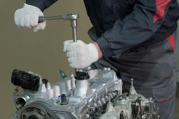 Repair of an automobile engine. An auto mechanic holds a tool in his hands and controls the fixation of the fastening nuts.