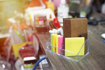 Office tool box on the desk, brown. In the box there is note paper ready for use. Around the desk are many things