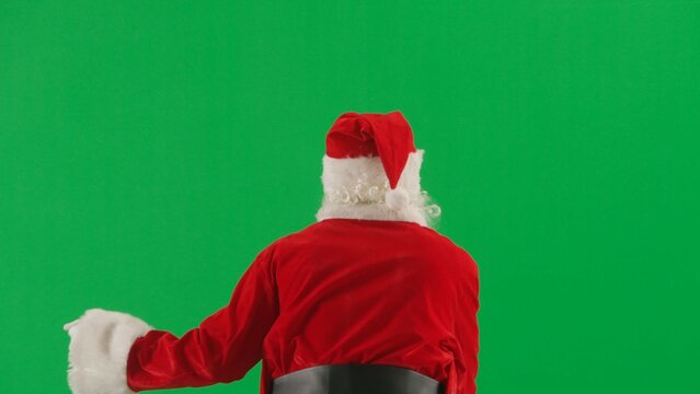 Portrait of man dressed as Santa on chroma key green screen background. Santa Claus in red outfit walking and greeting people around, waving. Back view. - Powered by Adobe