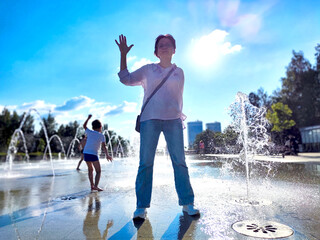 A person enjoys the refreshing splashes from fountains in a lively city park on a bright, sunny afternoon © keleny