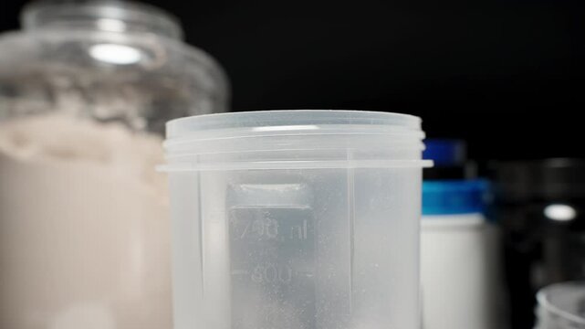 Athlete pouring a scoop of Protein Powder into a shaker bottle, adding the necessary supplement for muscle recovery. Slow motion.