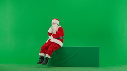 Obraz premium Portrait of man dressed as Santa on chroma key green screen background. Santa Claus in outfit sitting thinking, coming with idea positive mood.