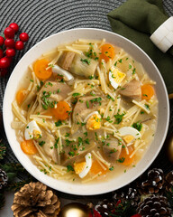 Noodle soup with carrots, artichokes and egg. Top view table with Christmas decoration.