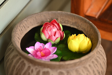 Colorful Lotus Blossoms in Stone Bowl: Vibrant Pink, Yellow, and Red Water Lilies Floating on Green Leaves in a Textured Gray Container, Creating a Serene Spa-like Atmosphere in Home Decor