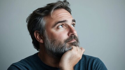 Obraz premium Thoughtful man with gray hair and beard contemplating while resting his chin on his hand in a neutral-toned setting