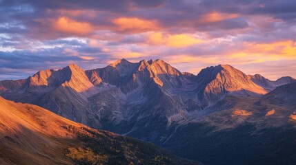 A dramatic sunrise over high mountain ranges, with the first light casting long shadows and illuminating the rugged peaks and valleys in warm hues.