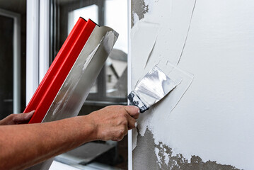 Woman plastering the walls with finishing putty in the room with putty knife or spatula.