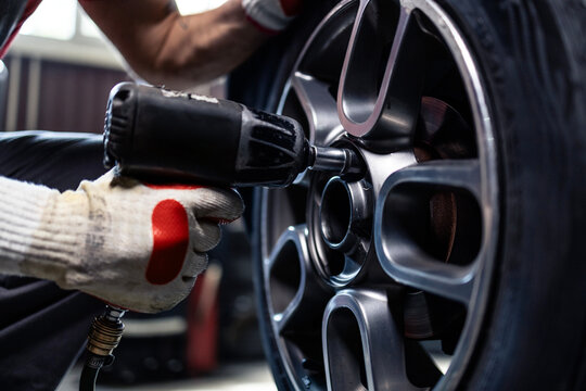 Removing wheels from vehicle with pneumatic impact wrench tool inside workshop.