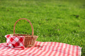 One picnic wicker basket with checkered napkin and blanket on green grass. Space for text