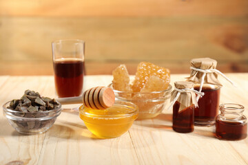 Honey, tincture, propolis granules and honeycombs on light wooden table, closeup. Alternative...