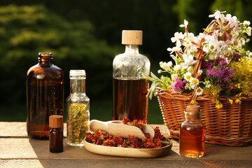 Tincture in bottles and different flowers on wooden table outdoors