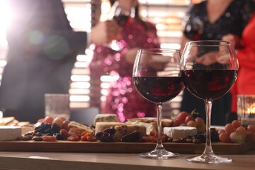 People holding glasses of wine at party, focus on wooden table with snacks and alcohol