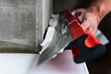 Woman plastering the walls with finishing putty in the room with putty knife or spatula.
