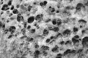 Black and white stone wall background.Grey rock with holes and potholes on surface. Monochrome abstract pattern. Rock texture backdrop. Element, material design. Close up.