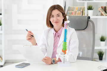 Young attractive female doctor orthopedist demonstrating the problem on spine bone model on the...