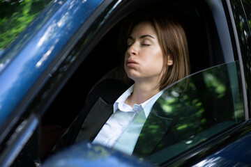 Young attractive businesswoman in suit driving and standing in a traffic jam. Tired business lady...