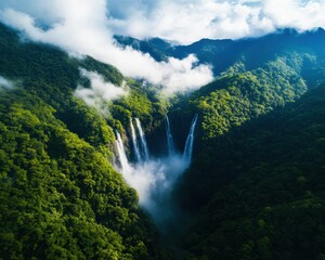 Fototapeta premium Stunning aerial view of a waterfall cascading through lush green mountains under a blue sky with fluffy clouds.