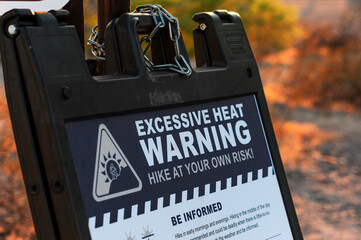 An 'Excessive Heat Warning: Hike at Your Own Risk!' sign stands near a hiking trail at A Mountain in Tempe, Arizona