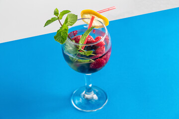 cocktail berry raspberry blueberry lemon and mint in a glass with a straw on a blue background top view