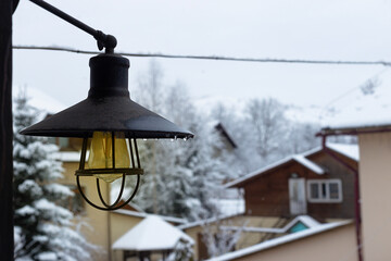 A rustic lamp hangs over a snowy landscape, capturing serene winter vibes in a mountain village...