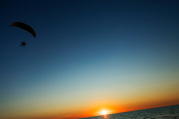 A person is joyfully parasailing high above the ocean during sunset
