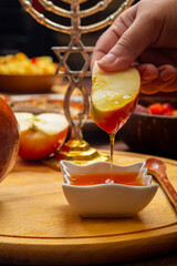 A woman's hand at a table with a menorah on the holiday of Rosh Hashanah dips an apple in honey
