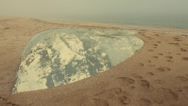 The seashore after a strong winter storm. The fishing boat was washed up on the shore, washed away by sand. Calm after the storm, foggy warm weather