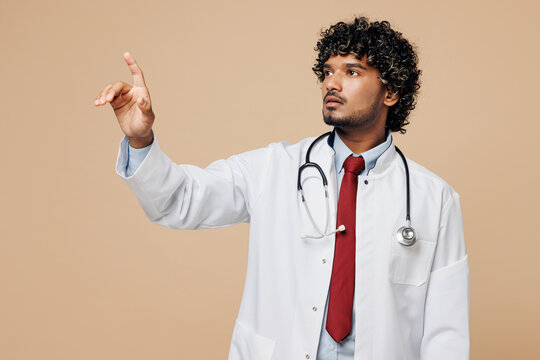 Young doctor man wear white medical gown suit work in hospital clinic office touch push click on button point at floating virtual screen isolated on plain beige background Healthcare medicine concept