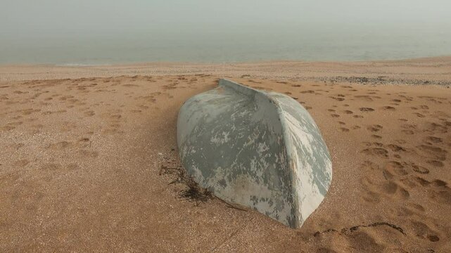 The seashore after a strong winter storm. The fishing boat was washed up on the shore, washed away by sand. Calm after the storm, foggy warm weather