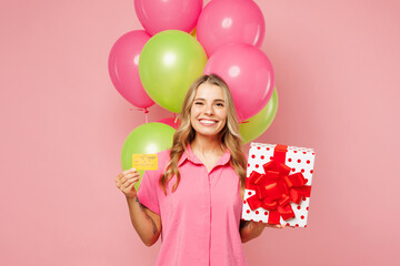 Young happy woman wear shirt celebrating birthday holiday stand near bunch of air balloons, hold...